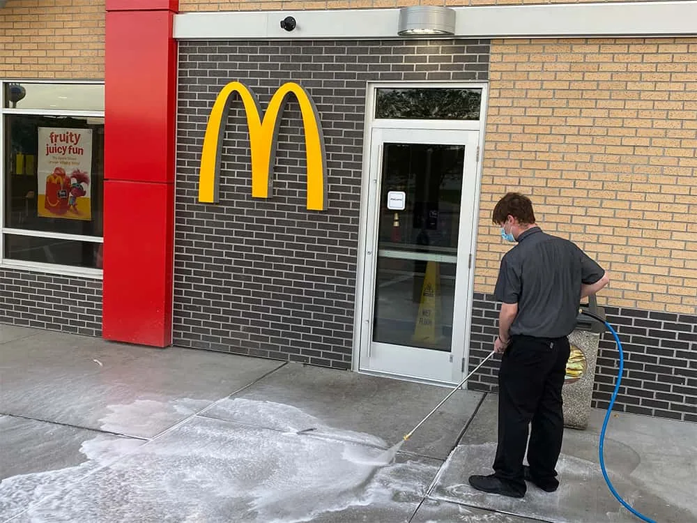 Crew member washing a quick-service restaurant exterior with an Easiwash hose cart